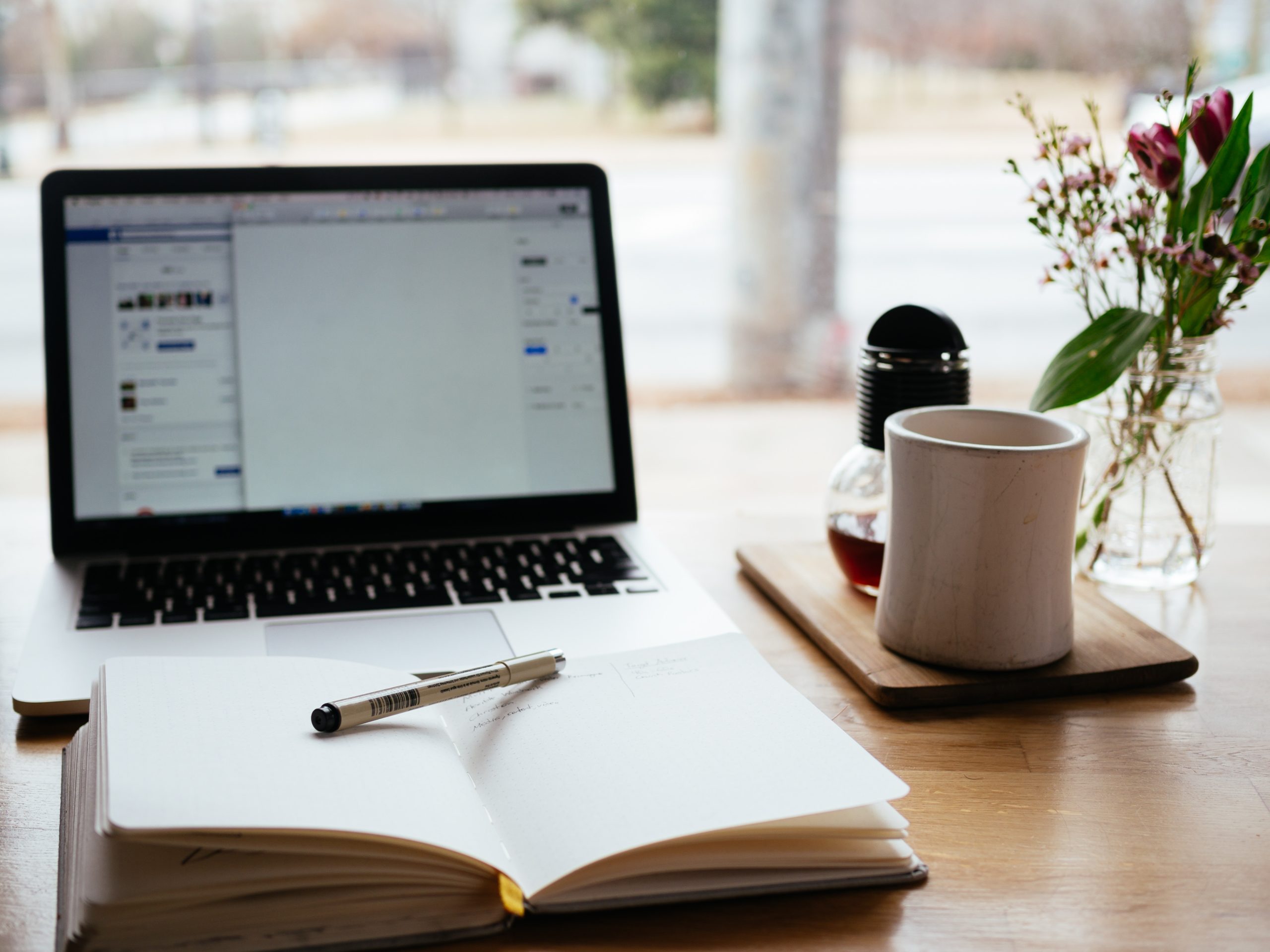 Laptop open next to a notebook and a mug