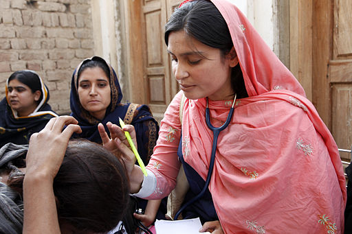 A woman healthcare provider, in traditional clothing is outside providing medical care.