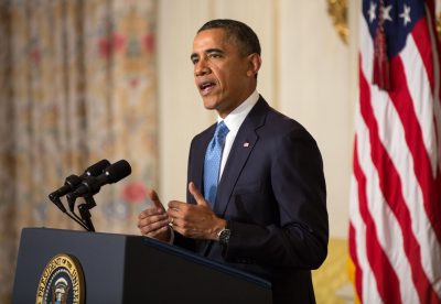 Former President Barack Obama is standing and speaking at a podium.