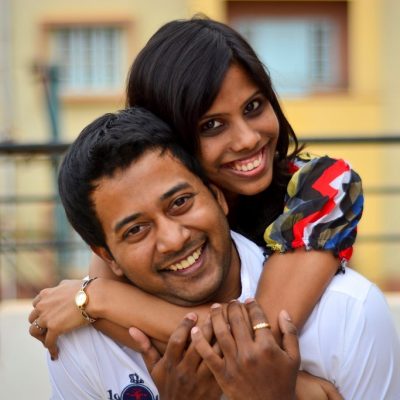 A smiling couple; the female has her arms wrapped around her partners neck.